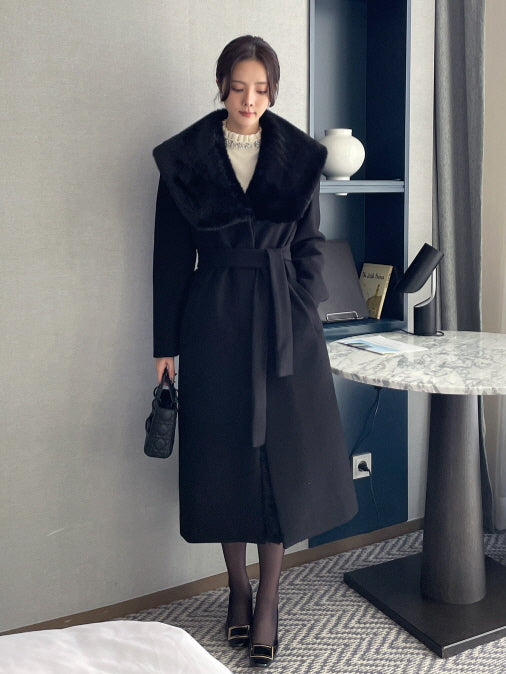 ブラックのフェイクファーカラー付きロングコートを着用したモデルの全身写真、ウエストベルトでくびれを作るきれいめエレガントな冬アウターコーデ。