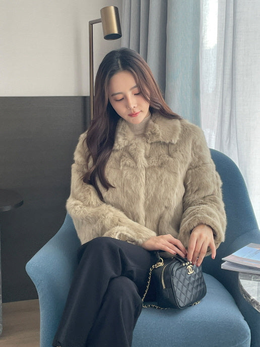 ベージュのフェイクファーショートコートを着た女性が椅子に座り、落ち着いた雰囲気で過ごしている上品なレディース冬スタイルの写真