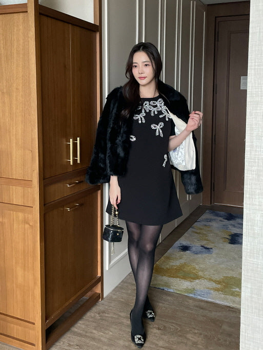 黒のフェイクファーショートコートをワンピースと合わせた女性がホテルの廊下で立っている、エレガントで華やかな冬のお出かけコーデ