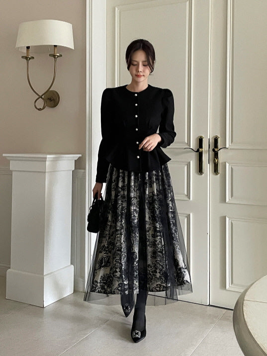 黒のジャケットとモノトーンのトワル柄チュールスカートを合わせた女性がドア前でポーズを取る全身スタイル。落ち着いた色合いと揺れるフレアラインがエレガントなクラシック系コーデ。