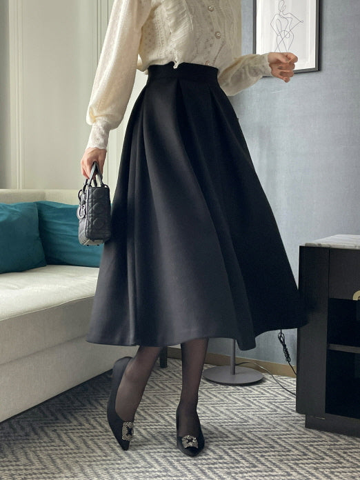 動くたびに広がる黒のハイウエストフレアスカートを主役に、アイボリーのレースブラウスと合わせたきれいめレディースコーデを室内で撮影したスタイリング写真。